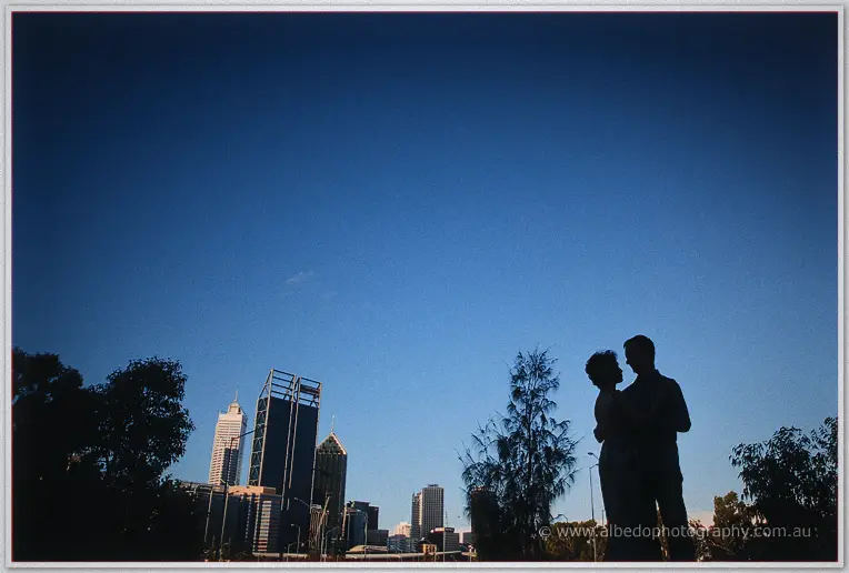 Loan and Alex stand silhouetted against deepening blue sky above the city towers