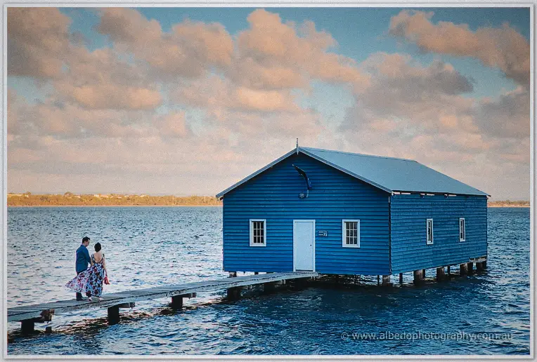 Loan and Alex walk the jetty toward the blue boat house on the river at sunset
