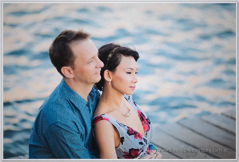 Loan and Alex sit side by side gazing across the water as soft light falls on their faces