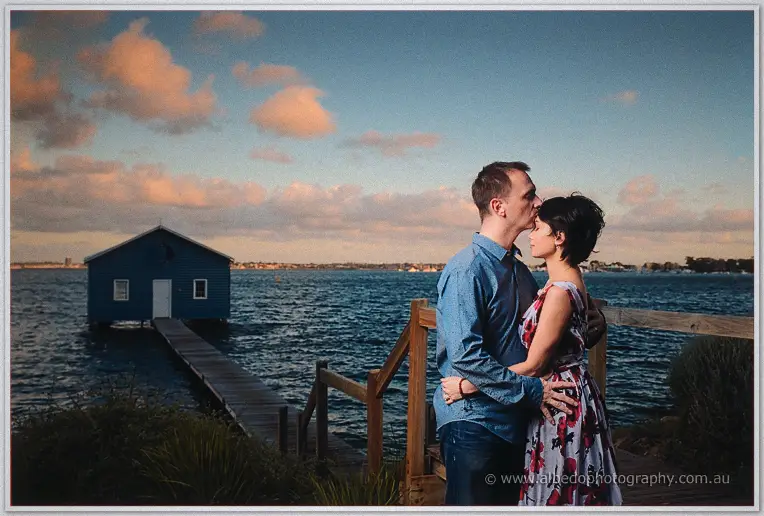 Alex kisses Loan's temple by the river stairs as pink clouds gather over the boat house
