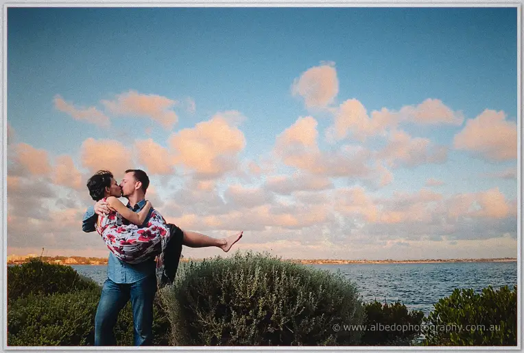 Alex swings Loan into a kiss on the coastal bushes beneath a big cloud-flecked evening sky