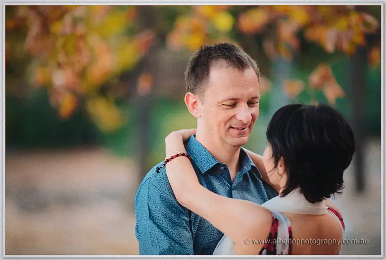 Loan wraps her arms around Alex's neck as he grins down at her under autumn leaves