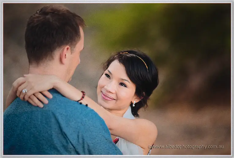 Loan beams up at Alex with her arms around his shoulders in soft evening light