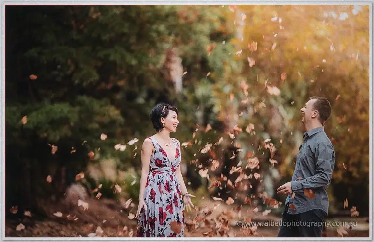Loan and Alex toss autumn leaves into the air and laugh among the golden trees