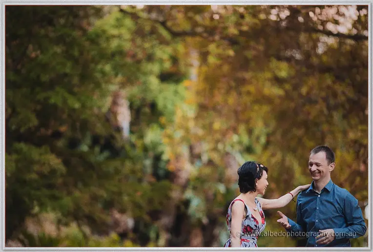 Loan touches Alex's shoulder as the pair grin at each other beneath sprawling autumn branches