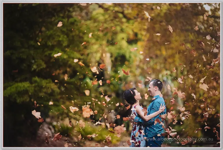 Loan and Alex embrace under a whirlwind of falling autumn leaves in the park