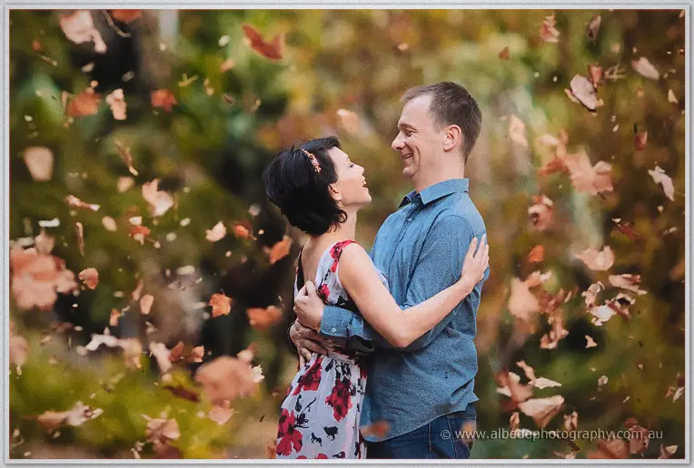 Loan and Alex laugh face to face as autumn leaves rain down around them