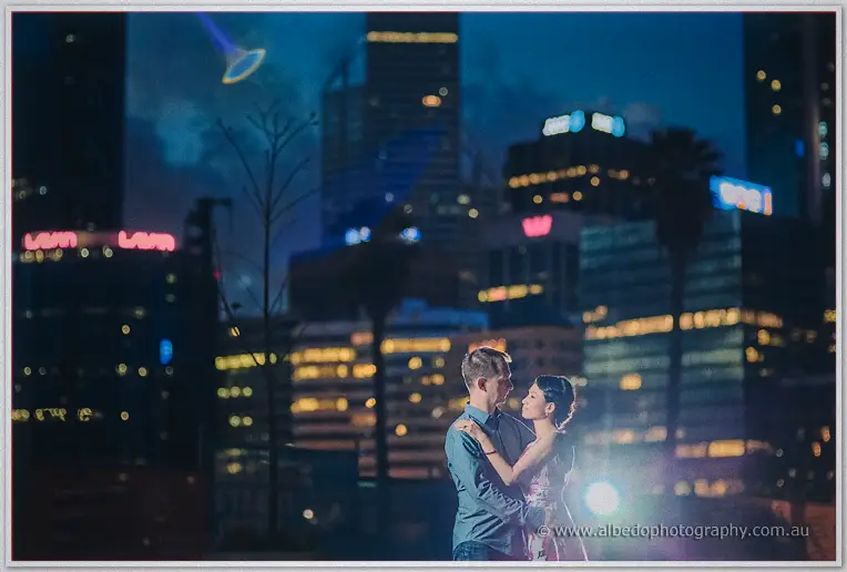 Loan and Alex embrace before the glowing Perth skyline at night from a hilltop lookout