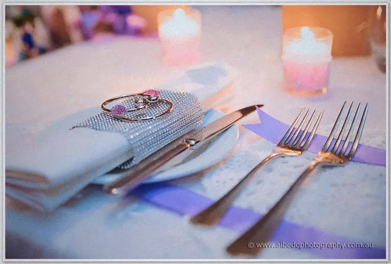 Place settings with rhinestone napkin rings, forks and purple ribbons glow by candlelight