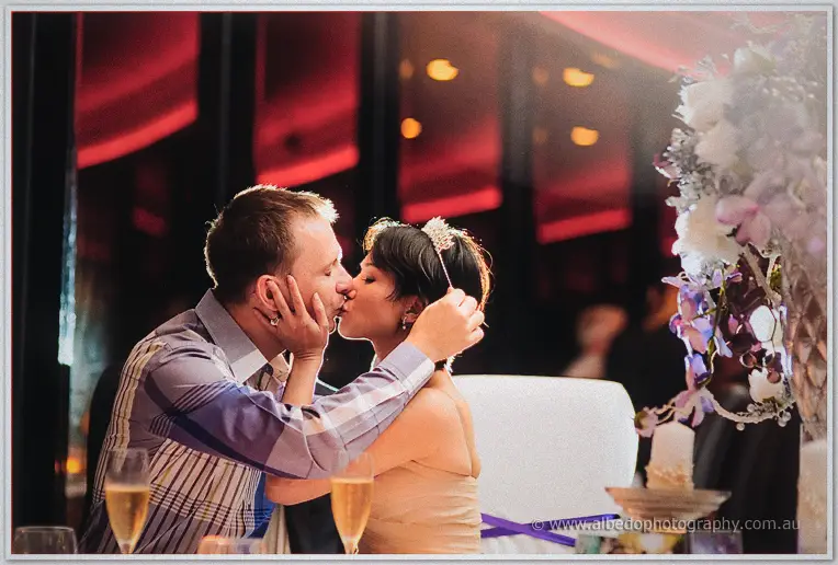 Loan cups Alex's face for a kiss at the head table after he crowns her with a tiara