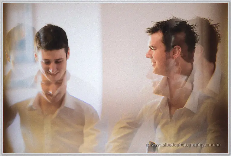 Softly blurred reflection shows two smiling groomsmen in white shirts during morning preparations