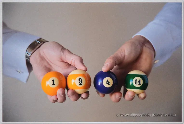 Groom and groomsman hold numbered billiard balls spelling out the wedding date between their hands