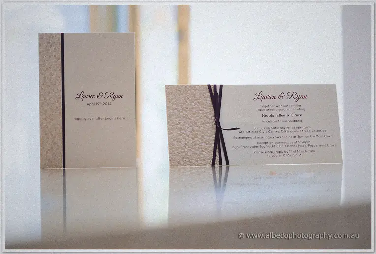 Lauren and Ryan's cream invitation cards with plum ribbon on a bright windowsill