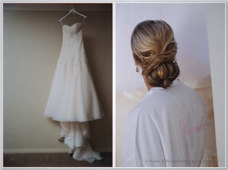 Strapless lace wedding dress on a hanger beside the bride's low chignon and white robe
