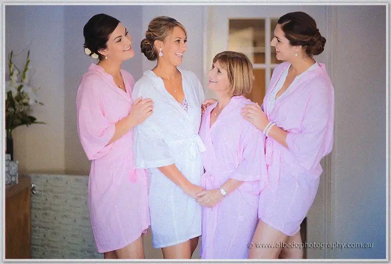 Bride in white robe laughs with three women in pink dressing gowns before the ceremony