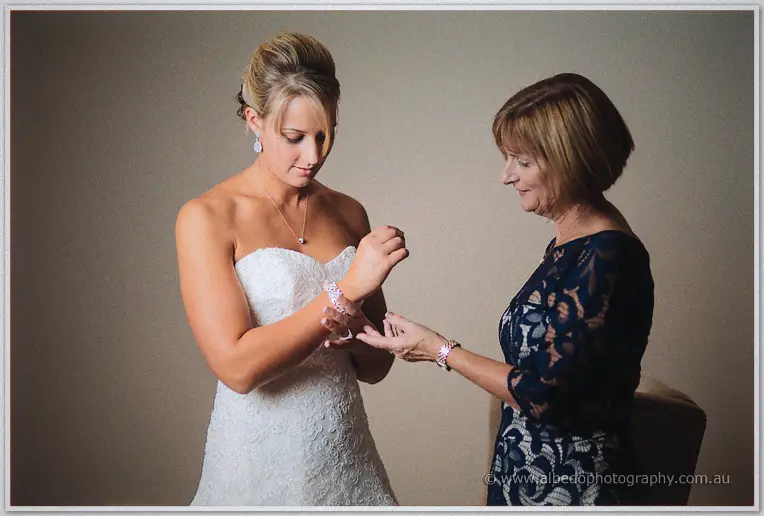 Lauren's mother in navy lace helps her fasten a sparkling bracelet in soft window light