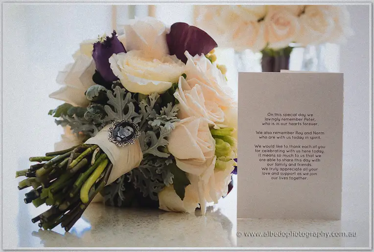 Bridal bouquet of cream roses and purple callas beside a card remembering family on the wedding day