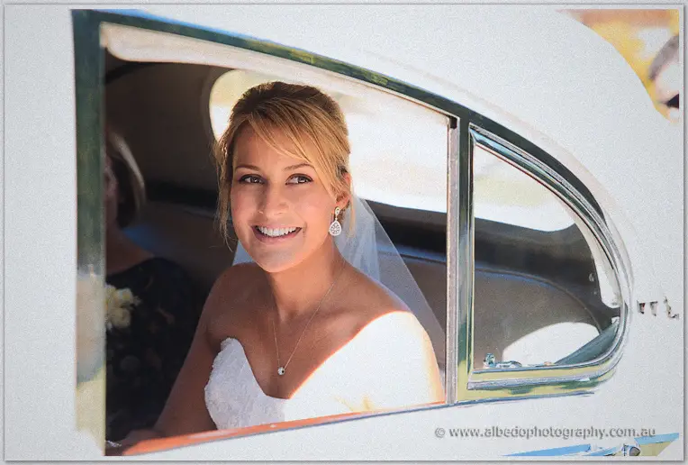 Lauren grins through the car window, veil catching the sun as she arrives