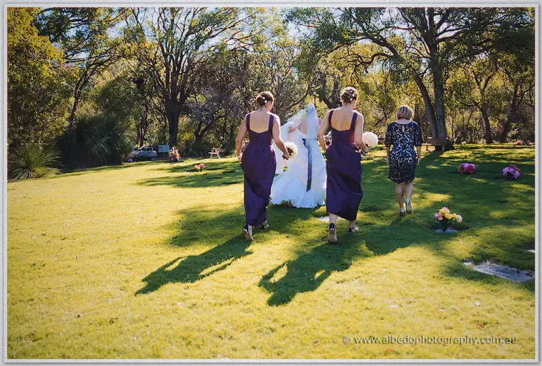 Lauren walks across a sunlit lawn with her bridesmaids and mother toward the ceremony