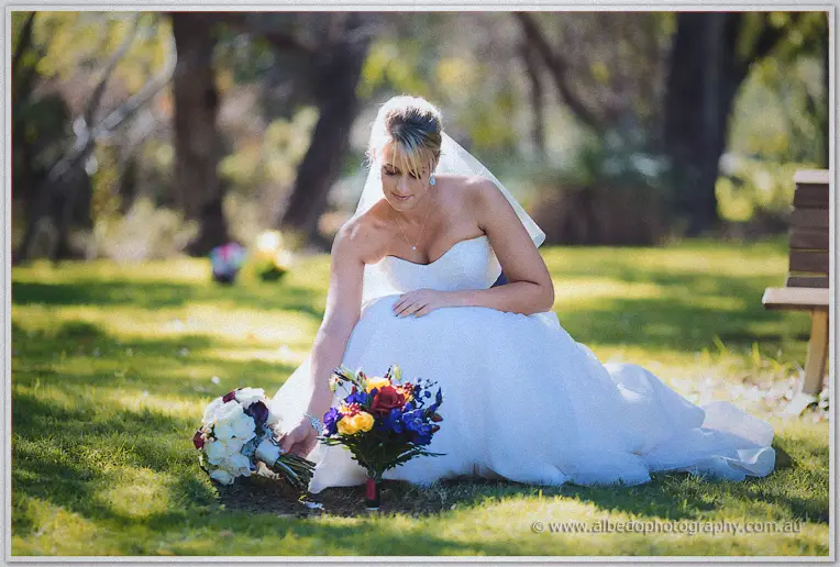 Lauren kneels on the grass arranging her bouquet beside bright memorial flowers