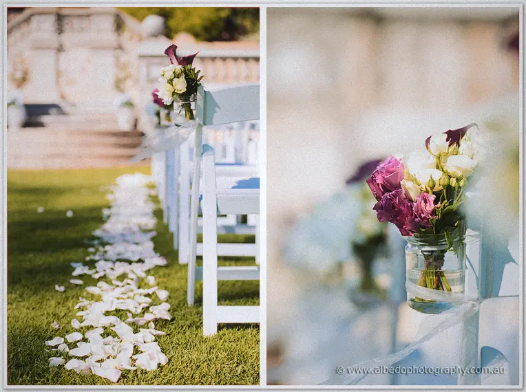 White petals line the grass aisle between chairs dressed with rose jars at Cottesloe