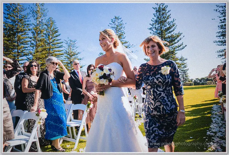 Lauren on her mother's arm during the processional, guests rising along the chair rows