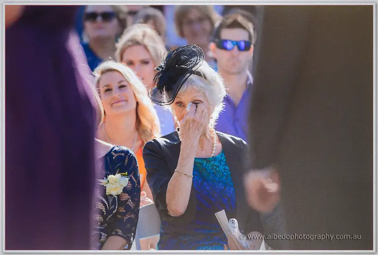 A grandmother in a black fascinator dabs away tears as vows are read