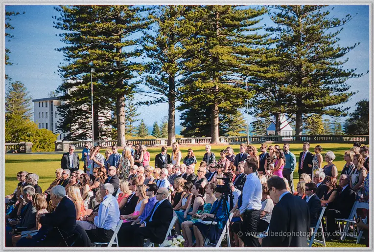 Guests fill the lawn ceremony beneath pines with the Cottesloe coastline beyond