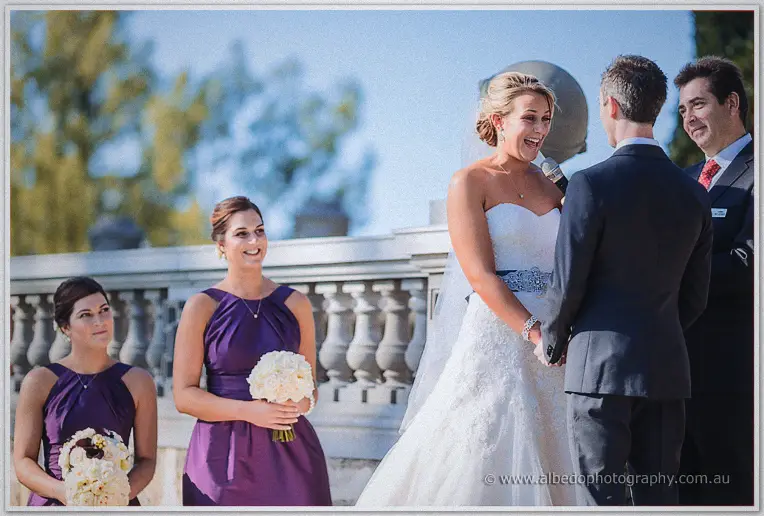 Lauren laughs mid-vow holding Ryan's hands, bridesmaids and celebrant close by