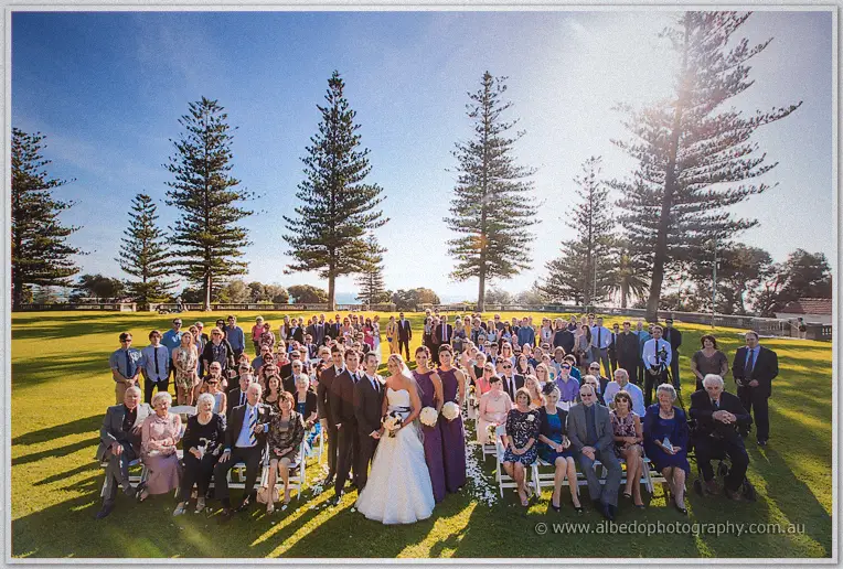 Lauren and Ryan front a full group photo on the lawn beneath towering pines