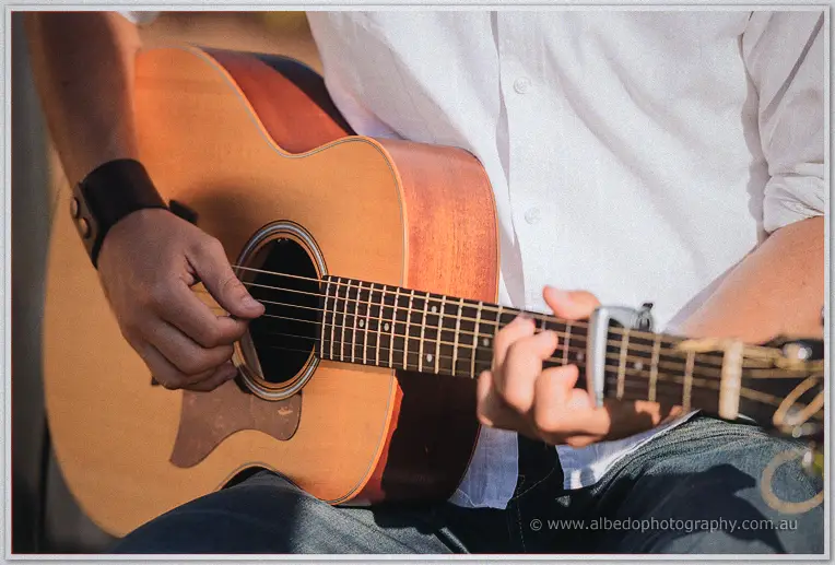 Close-up of hands strumming an acoustic guitar fitted with a capo in the sun