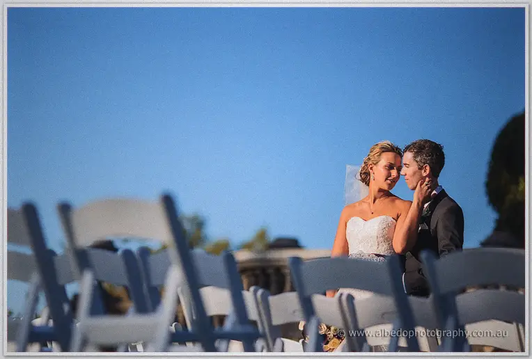 Lauren strokes Ryan's face between empty chairs under a deep blue sky