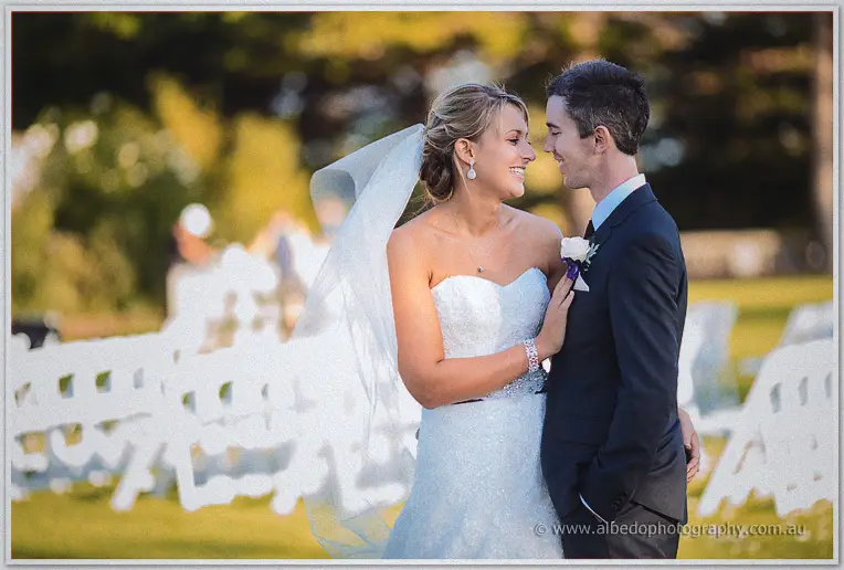 Lauren and Ryan laugh face to face among white chairs in low golden light