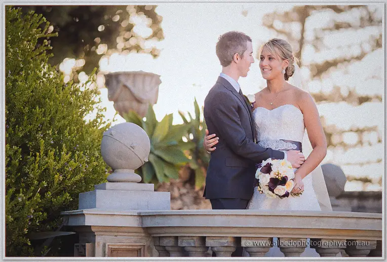 Ryan and Lauren share a quiet moment on a stone balcony, her plum and cream bouquet catching soft light