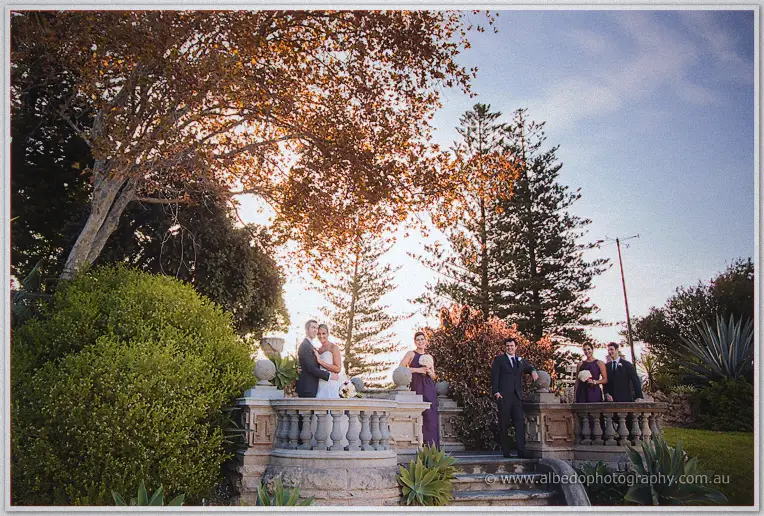 The wedding party gathers on Cottesloe's stone steps at golden hour under autumn-toned trees