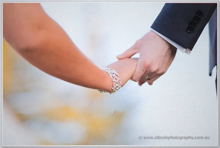 Close-up of Ryan holding Lauren's bracelet-adorned hand against soft blurred garden light