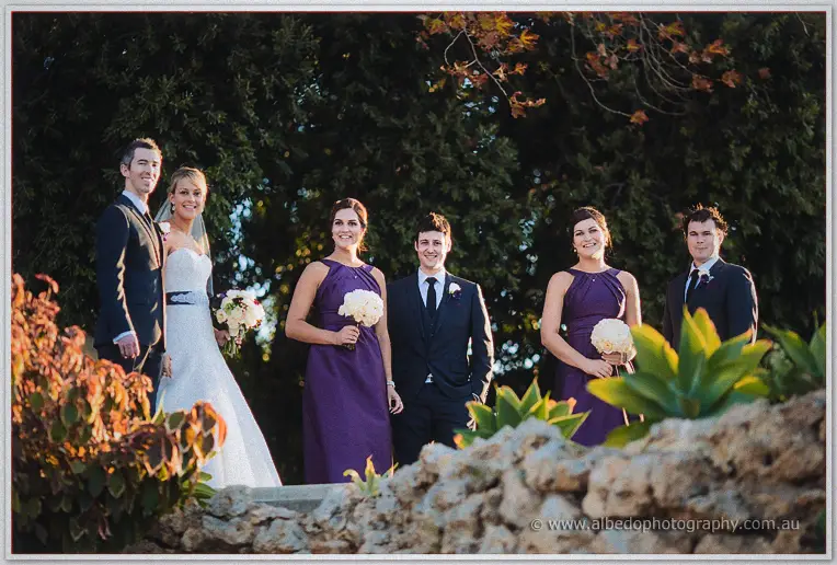 The full wedding party stands among autumn foliage and limestone rocks in soft evening light