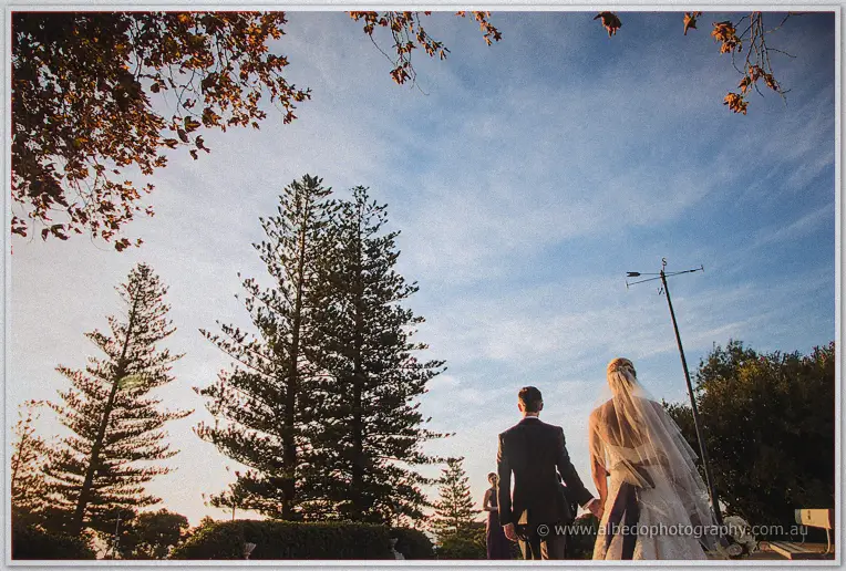 Lauren and Ryan walk hand in hand beneath tall pines and autumn leaves toward the setting sun