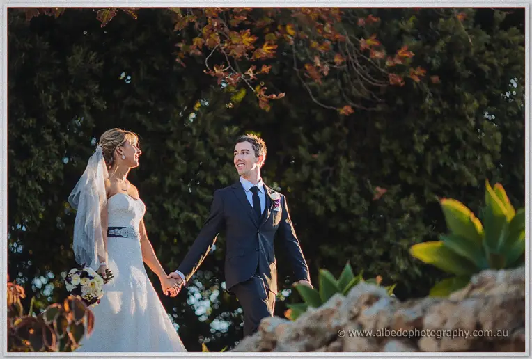 Lauren and Ryan grin at each other mid-stride past succulents and limestone in golden light