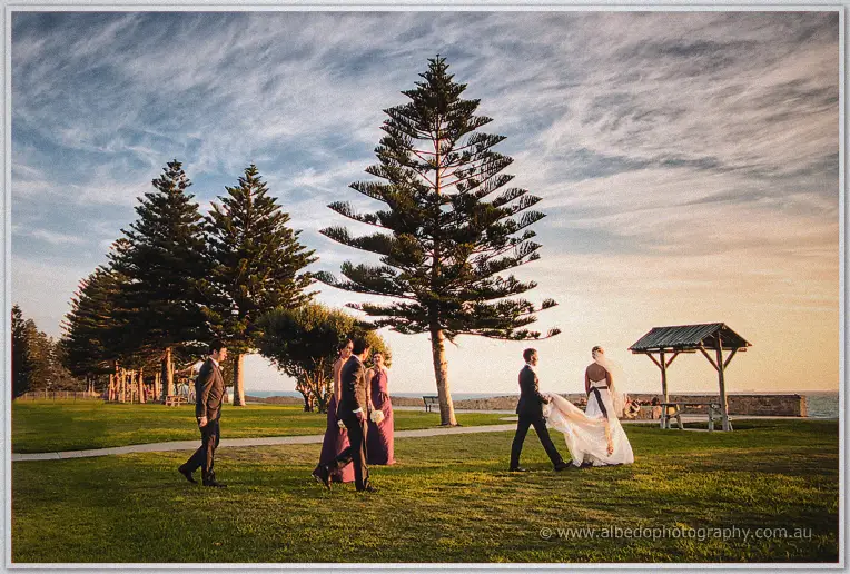 The wedding party crosses the Cottesloe foreshore at sunset, groomsman trailing Lauren's veil
