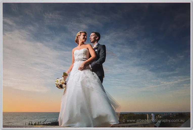 Lauren and Ryan embrace above the Indian Ocean, her bouquet in hand under a glowing dusk sky