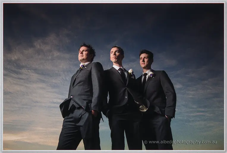 Ryan and his groomsmen stand shoulder to shoulder in charcoal suits under a darkening sky