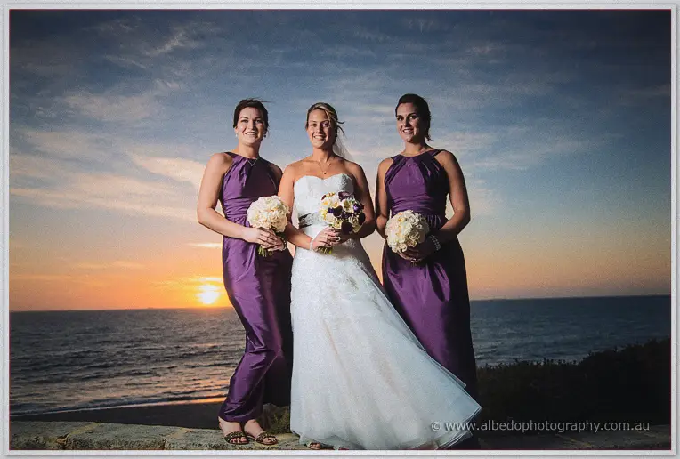 Lauren and her bridesmaids hold cream bouquets as the sun sets behind them over the ocean