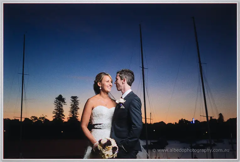 Lauren and Ryan smile at each other in the yacht club marina as dusk silhouettes the masts