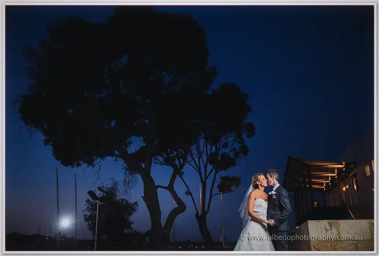 Lauren and Ryan kiss beneath a ghostly gum tree under a deep blue evening sky by the water