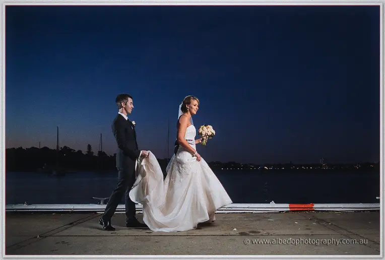 Ryan carries Lauren along the jetty at night, her train sweeping the marina boards