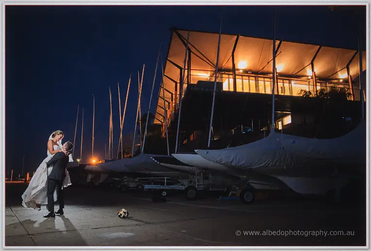 Ryan dips Lauren for a kiss outside the lit boatshed, dinghies stacked along the wall