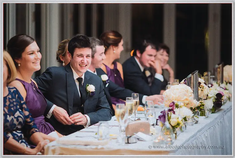 The bridal table bursts into laughter, champagne flutes and white roses lining the cloth