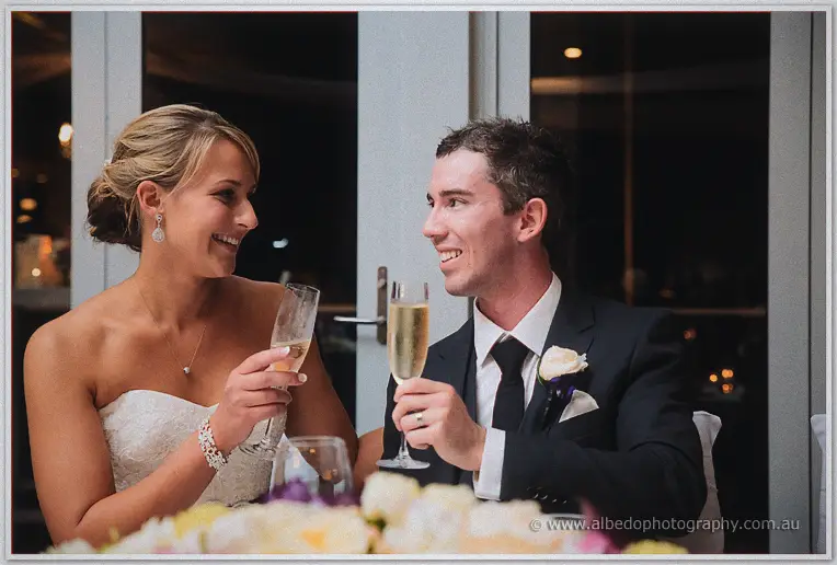 Lauren and Ryan raise champagne flutes, grinning at each other across the candlelit table