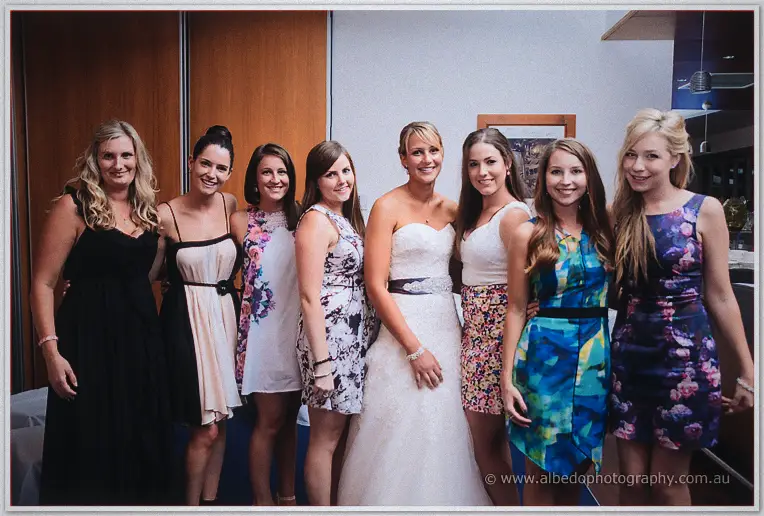 Lauren in her strapless gown posing arm in arm with eight female friends in colourful cocktail dresses indoors
